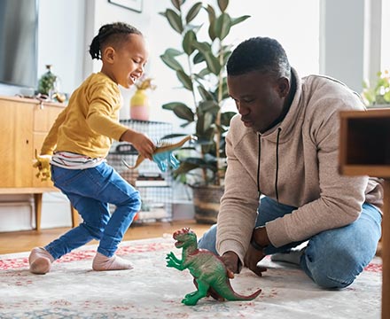 Dad and child playing with a dinosaur at home.