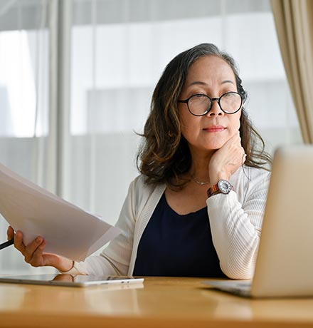 Woman with papers looking at her laptop.